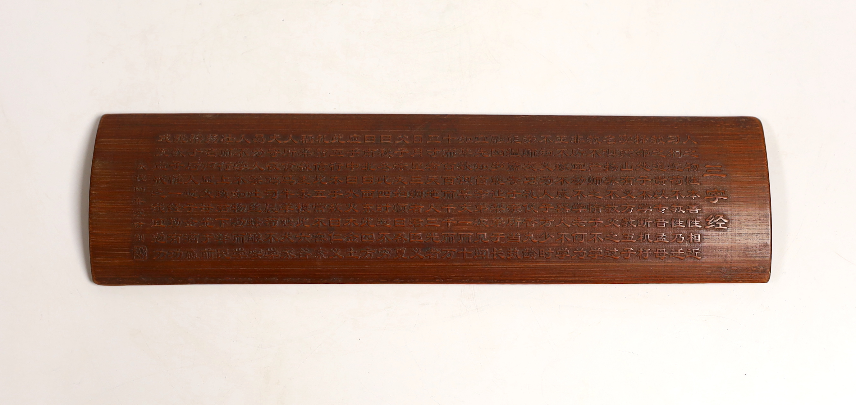 A Chinese bamboo inscribed wrist rest, carved in relief with columns of calligraphy, 30cm wide
